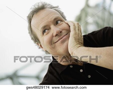 Picture - Close-up of a mature man with his hand on his chin and smiling. Fotosearch