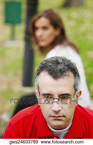 Close-up of a mid adult man looking sad with a mid adult woman sitting behind him View Large Photo Image Stock Photo - Close-up of a mid adult man looking sad with a mid adult woman sitting behind him. Fotosearch