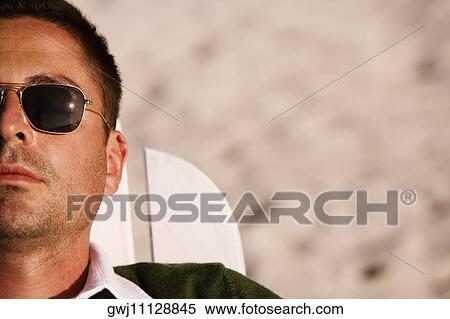 Close-up of a mid adult man reclining on a lounge chair View Large Photo Image Stock Photography - Close-up of a mid adult man reclining on a lounge chair. Fotosearch
