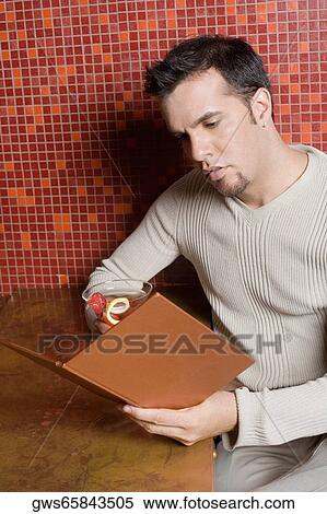 Close-up of a mid adult man sitting at a bar counter holding a cocktail and reading a menu View Large Photo Image Stock Photography - Close-up of a mid adult man sitting at a bar counter holding a cocktail and reading a menu. Fotosearch