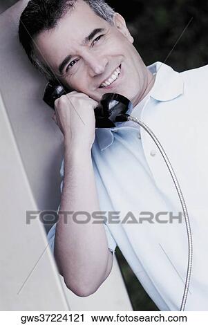 Stock Image - Close-up of a mid adult man talking on a pay phone. Fotosearch