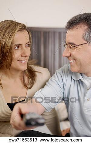 Stock Image - Close-up of a mid adult man using a remote control beside a mid adult woman. Fotosearch
