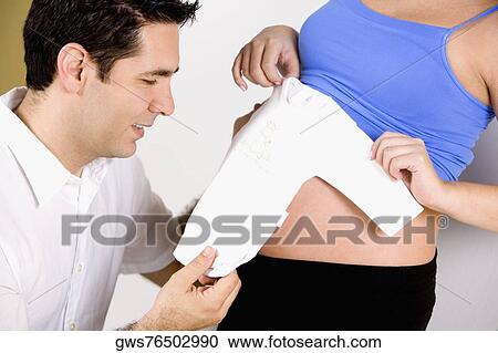 Close-up of a mid adult man watching an onesie with a pregnant woman holding it View Large Photo Image Stock Image - Close-up of a mid adult man watching an onesie with a pregnant woman holding it. Fotosearch