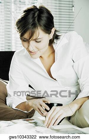 Stock Image - Close-up of a mid adult woman reading a magazine on the bed. Fotosearch