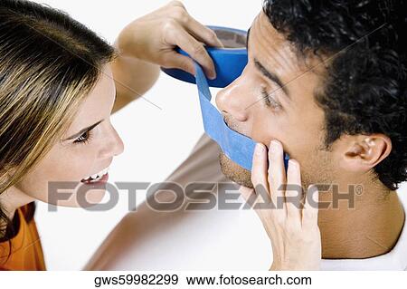 Close-up of a mid adult woman sticking an adhesive tape on a young man's mouth View Large Photo Image Stock Photo - Close-up of a mid adult woman sticking an adhesive tape on a young man's mouth. Fotosearch