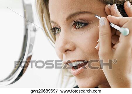 Stock Photo - Close-up of a mid adult woman tweezing her eyebrows. Fotosearch