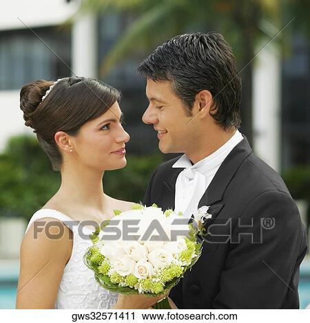 Close-up of a newlywed couple holding a bouquet of flowers and looking at each other View Large Photo Image Stock Image - Close-up of a newlywed couple holding a bouquet of flowers and looking at each other. Fotosearch