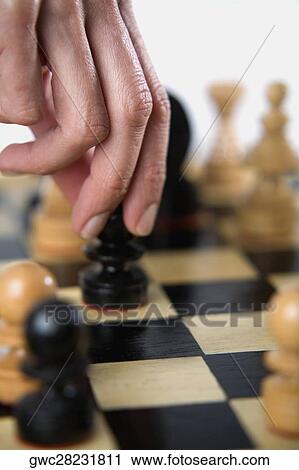 Stock Image - Close-up of a person's finger holding a chess piece. Fotosearch