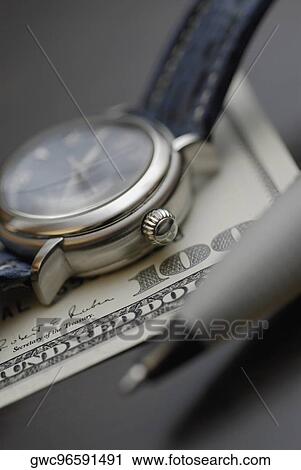 Stock Image - Close-up of a wristwatch with a pen on an one hundred dollar bill. Fotosearch
