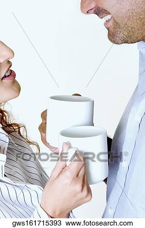 Stock Image - Close-up of a young couple holding coffee cups and smiling. Fotosearch