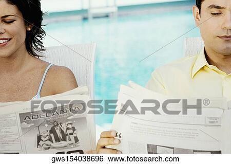 Stock Photograph - Close-up of a young couple reading newspapers at the poolside. Fotosearch