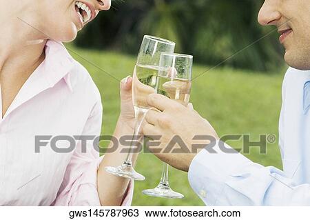 Stock Image - Close-up of a young couple toasting with champagne flutes. Fotosearch