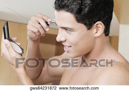 Stock Image - Close-up of a young man applying blush. Fotosearch