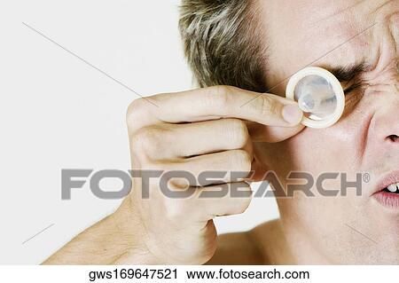 Close-up of a young man holding a condom in front of his eye View Large Photo Image Stock Image - Close-up of a young man holding a condom in front of his eye. Fotosearch