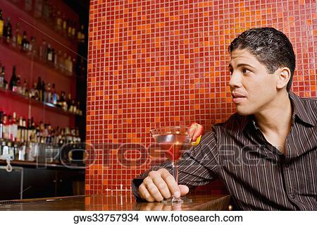 Close-up of a young man sitting at a bar counter and holding a cocktail View Large Photo Image Picture - Close-up of a young man sitting at a bar counter and holding a cocktail. Fotosearch