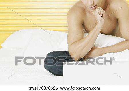 Close-up of a young man sitting on the bed in front of a laptop View Large Photo Image Stock Photography - Close-up of a young man sitting on the bed in front of a laptop. Fotosearch