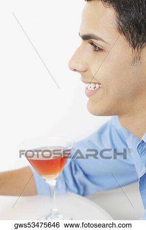 Close-up of a young man smiling with a glass of martini in front of him View Large Photo Image Stock Photograph - Close-up of a young man smiling with a glass of martini in front of him. Fotosearch