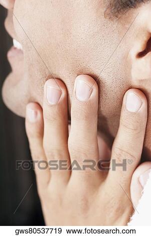 Close-up of a young man touching his face View Large Photo Image Stock Photo - Close-up of a young man touching his face. Fotosearch