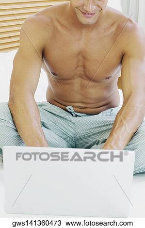 Close-up of a young man using a laptop on the bed View Large Photo Image Stock Image - Close-up of a young man using a laptop on the bed. Fotosearch