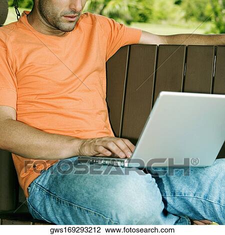 Close-up of a young man using a laptop on a porch swing View Large Photo Image Stock Image - Close-up of a young man using a laptop on a porch swing. Fotosearch