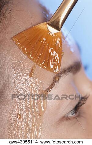 Picture - Close-up of a young woman applying a facial mask. Fotosearch