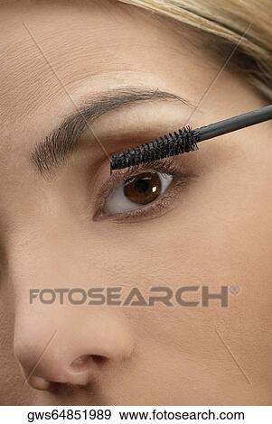 Stock Photo - Close-up of a young woman applying mascara on her eyelashes. Fotosearch
