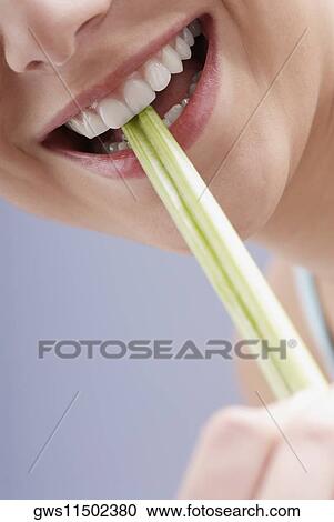 Stock Image - Close-up of a young woman biting celery sticks. Fotosearch
