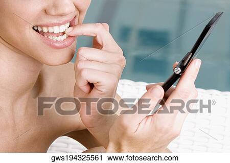 Close-up of a young woman holding a mobile phone and smiling View Large Photo Image Stock Image - Close-up of a young woman holding a mobile phone and smiling. Fotosearch