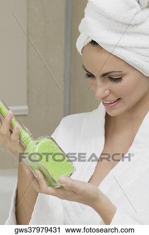Stock Image - Close-up of a young woman holding a bottle of bath crystals. Fotosearch