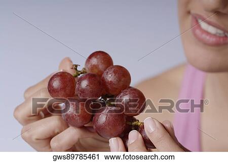 Stock Image - Close-up of a young woman holding a bunch of red grapes. Fotosearch