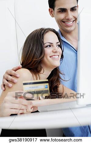 Stock Photo - Close-up of a young woman holding a credit card with a young man looking at a laptop. Fotosearch