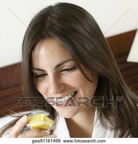 Stock Photo - Close-up of a young woman holding a cupcake and smiling. Fotosearch