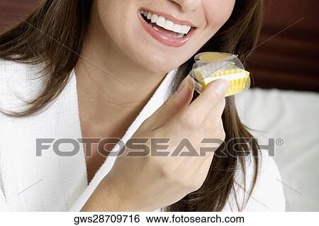 Stock Photograph - Close-up of a young woman holding a cupcake and smiling. Fotosearch