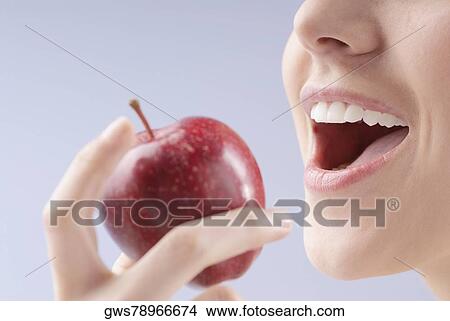 Picture - Close-up of a young woman holding an apple close to her mouth. Fotosearch
