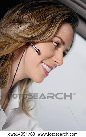 Stock Image - Close-up of a young woman wearing a hands free device and listening to music. Fotosearch