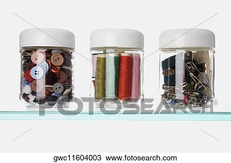 Stock Image - Close-up of buttons and safety pins with thread spools in three different jars. Fotosearch