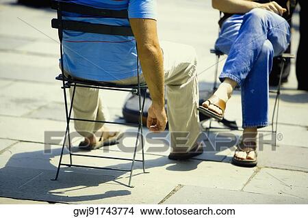 Close-up of two people sitting on chairs View Large Photo Image Picture - Close-up of two people sitting on chairs. Fotosearch