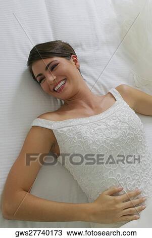 Stock Image - High angle view of a bride lying on the bed and smiling. Fotosearch