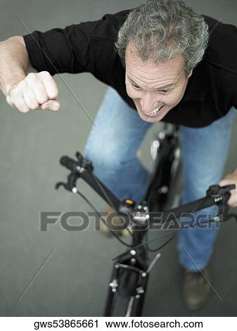 Stock Image - High angle view of a mature man cycling with his hand raised. Fotosearch