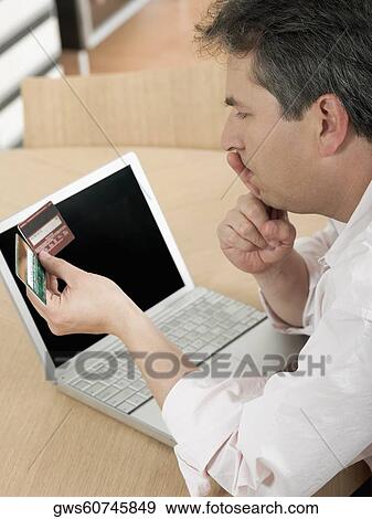 Stock Photo - High angle view of a mature man holding two credit cards and thinking. Fotosearch