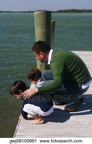 High angle view of a mid adult man with his son and daughter crouching on a pier and looking into the water View Large Photo Image Stock Image - High angle view of a mid adult man with his son and daughter crouching on a pier and looking into the water. Fotosearch