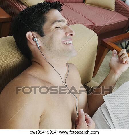 High angle view of a young man sitting in an armchair listening to music View Large Photo Image Picture - High angle view of a young man sitting in an armchair listening to music. Fotosearch