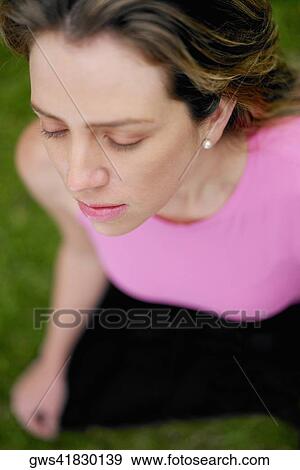 Stock Photo - High angle view of a young woman sitting in the lotus position. Fotosearch