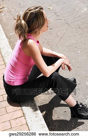 Stock Photograph - High angle view of a young woman sitting on a ledge. Fotosearch