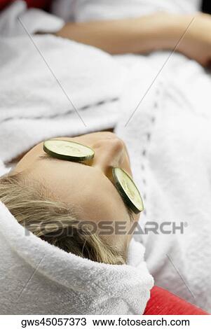 Stock Image - High angle view of a young woman with cucumber slices on her eyes. Fotosearch