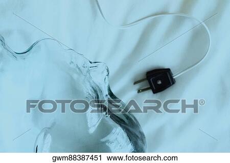 Stock Image - High angle view of an electric plug with a glass statue on a sheet. Fotosearch