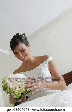 Stock Image - Low angle view of a bride looking at a bouquet of flowers. Fotosearch
