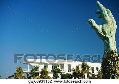Stock Image - Low angle view of a hand sculpture near a building. Fotosearch