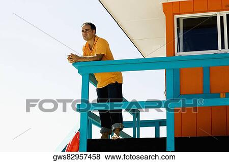 Low angle view of a mid adult man leaning against a railing of a lifeguard hut View Large Photo Image Stock Photo - Low angle view of a mid adult man leaning against a railing of a lifeguard hut. Fotosearch