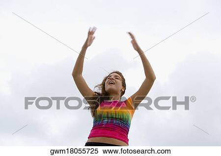Stock Photography - Low angle view of a mid adult woman with arms raised standing. Fotosearch